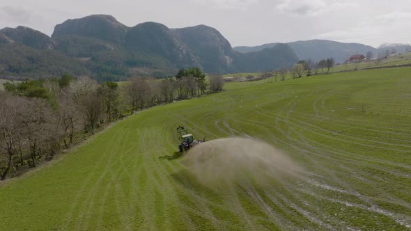 Tractor on scenic farm spraying organic fertilizer on pasture; aerial alt