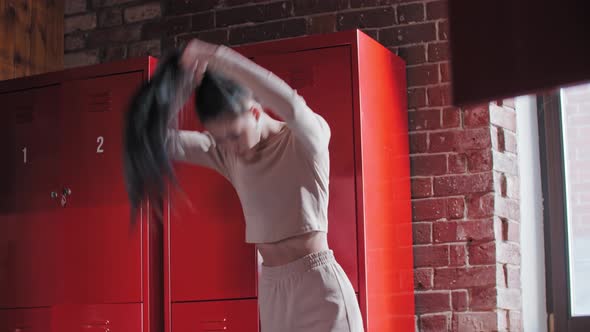 A Young Woman Putting Her Hair in Ponytail in Gym Changing Room alt