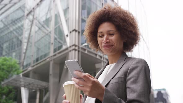 Afro American businesswoman in city using smart phone with takeaway coffee