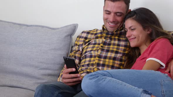 Cute couple using mobile phone in living room at home 4k