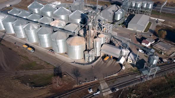 Truck Full of Grain Rides Near Large Metal Silos of Grain Elevator on Sunny Day alt