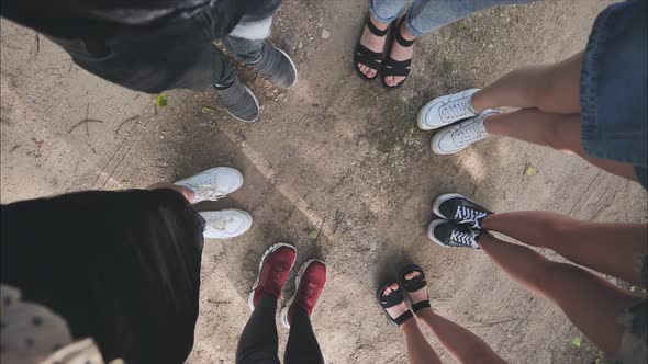 Legs and Sneakers of Teenage Boys and Girls Standing in Half Circle on the Sand alt