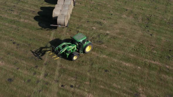 Aerial Agricultural shot of a Tractor collecting bales of Hay and loading them on a dispatched trail alt