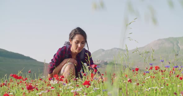 Smiling Woman Smelling and Picking Flowers From Field alt