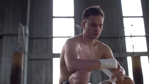 Portrait of Handsome Muscular Guy with Naked Torso Wrapping His Hands with Bandage in Sports Hall alt