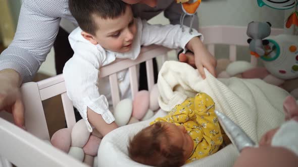 Dad and Son are Standing at the Crib with a Newborn Baby alt
