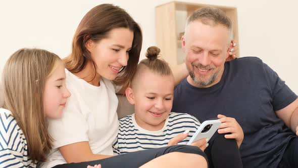 Happy Family Looking at Smartphone They are Sitting on the Couch and Smiling alt