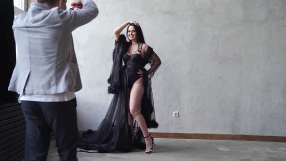 Sexy Woman in Black Bodysuit and Negligee Stands at Gray Wall