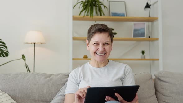 Smiling Elderly Mature Woman Resting on Sofa Using Digital Tablet Alone at Home alt