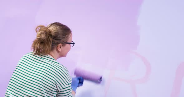 Young Woman in Glasses Tries to Paint Over Writing on Wall