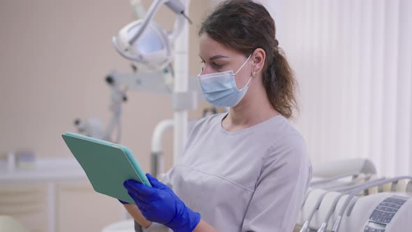 Professional Woman in Face Mask Examining Dental Xray on Tablet Standing in Office alt