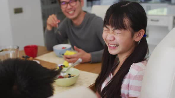 Happy asian father in kitchen eating breakfast with laughing son and daughter alt