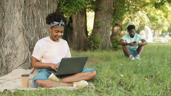 Cheerful Afro-American Woman Using Laptop in Park alt