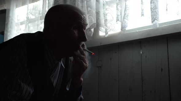 Silhouette of an Old Man Smoking on the Background of a Window alt