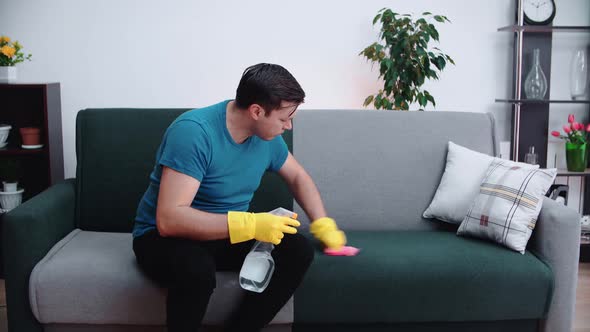 A man thoroughly cleans the sofa in the room with a rag and a cleaning agent