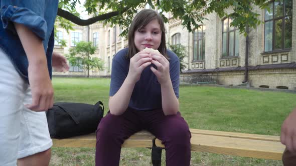 Relaxed Plump Boy Sitting on Bench with Sandwich As Unrecognizable Aggressive Classmates Knocking alt