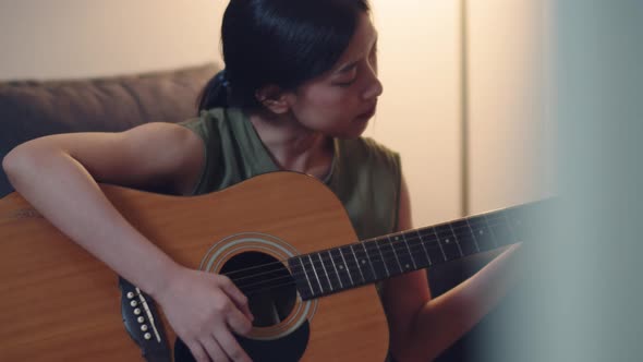 Asian female learning to play guitar at home while quarantined.