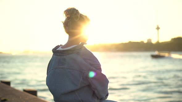 Slowmotion of Attractive Young Fairhaired Woman with Blue Eyes Sitting on Concrete Floor of Docks alt