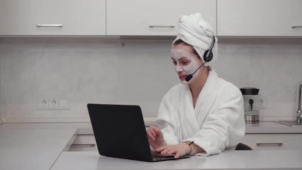 A Girl in a Robe in a Headset Headphone Talking Cheerfully on the Webcam