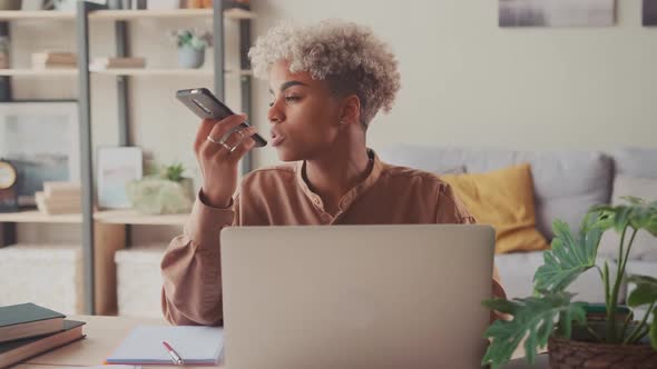 Focused Ethnic Female Employee Buys with Laptop Talk on Loudspeaker on Phone alt