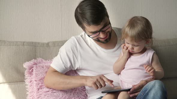 Happy Family Father with Little Daughter Watch Educational Games on Smartphone Sitting on Sofa