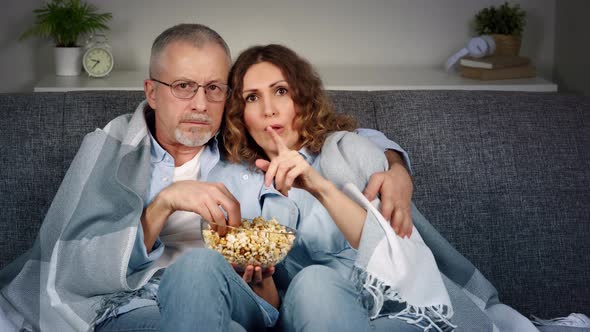 A Middleaged Couple is Watching a Horror Movie on TV and Eating Popcorn on the Couch