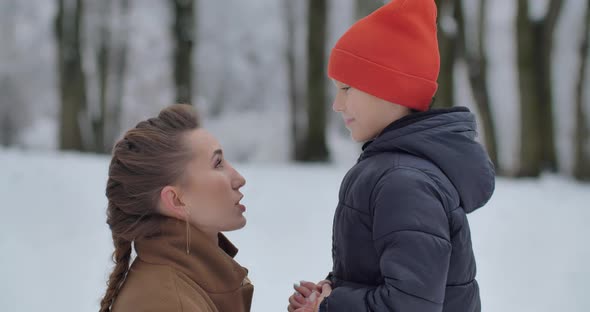 A Little Boy And His Mother Are Walking In A Snowy Park. The Boy Kisses His Mother Tenderly alt