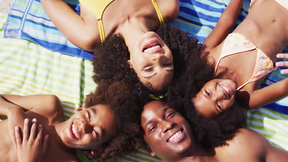Portrait of african american parents and two children lying on a towel at the beach smiling alt