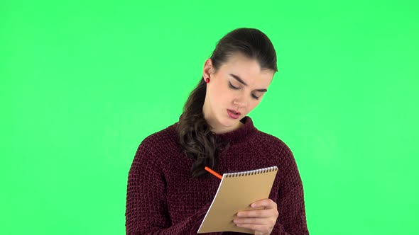 Girl Stands and Thinks, Then Angrily Writes with Pencil in Notebook. Green Screen alt
