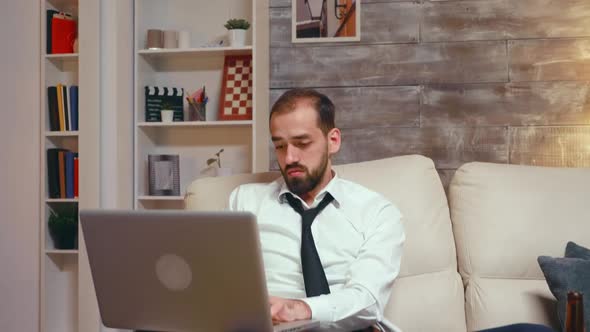 Tired Businessman in Living Room Working on Laptop alt