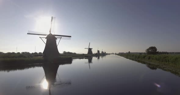 A drone shot panning left, around Dutch Windmills during sunrise alt