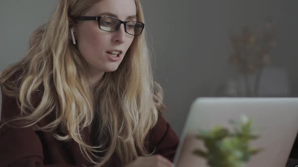 Businesswoman Making Video Call Using Laptop Looking at Screen Wearing Pods and Smiling alt