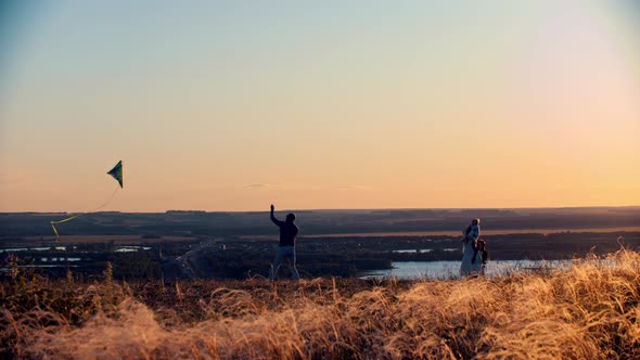 Young Family Playing with Kite on the Field on Sunset - Father Leading the Kite alt