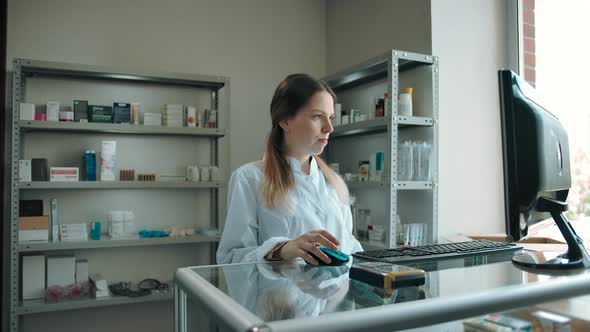 Young Saleswoman Looks at the Camera in the Interior of the Pharmacy alt