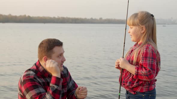 Father Showing Fish Bait To Daughter Near Lake