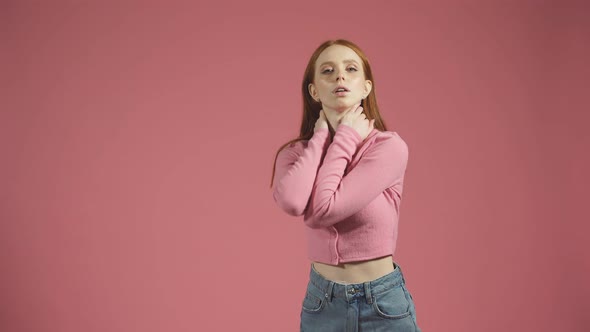Serious Young Model with Long Red Hair Poses for the Camera on an Isolated Pink Background in the