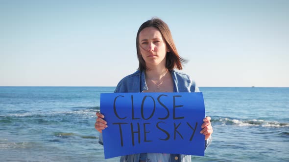 Upset ukrainian female holding blue banner with inscription Close The Sky alt
