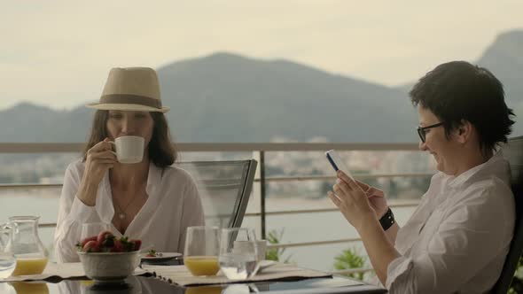 Mature Woman in a Cafe Takes Pictures of Friend for Social Network alt