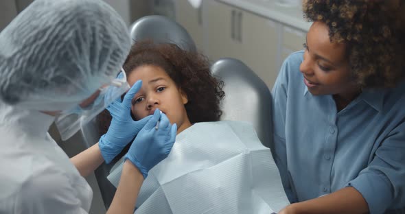 African Mother Sitting in Dental Office with Cute Little Daughter Having Teeth Checked alt