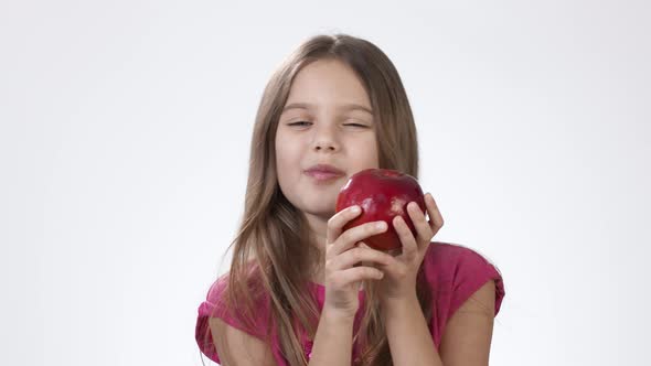 Little Girl on White Eats a Big Red Apple. A Girl Bites a Piece of Red Ash and Tastes It. alt