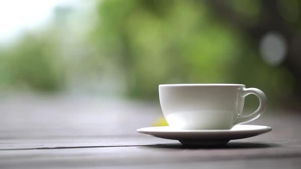 Hot coffee cup with smoke on wood table top in bokeh green nature background