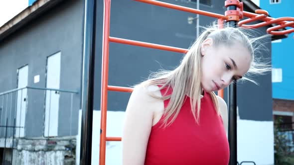 Young Blond Busty Woman with Ponytail in Red Top Stretches Neck at Sports Ground