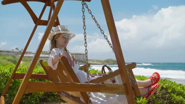 Smiling Woman Swinging on Wooden Swing in Beach Resort with Scenic Ocean Views alt