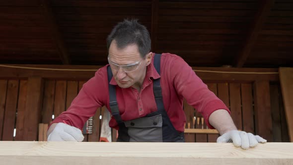 Worker in Goggles Makes Notes with Carpenters Pencil on a Wooden Blank alt
