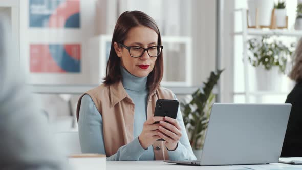 Businesswoman Surfing the Net on Smartphone at Office Desk alt