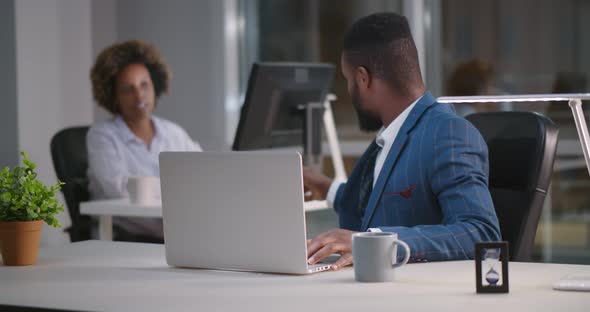 African Colleagues Talking Sitting at Desktop and Working on Computer Late at Work alt