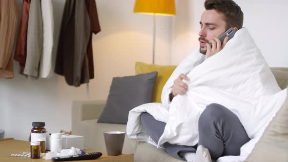 Sick Man Wrapped in Blanket Calling Doctor on Mobile Phone alt
