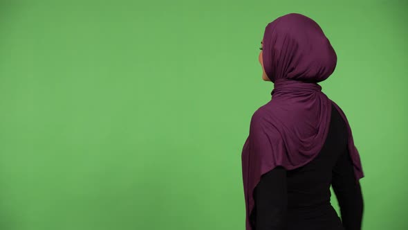 A Muslim Woman Cheers and Looks at the Green Screen Background with Her Back to the Camera