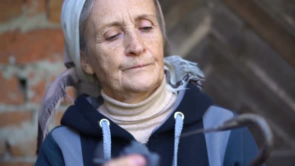Happy Beautiful Senior Woman is Holding Metal Hoe and Making It Clean After Work and Weeding in the alt