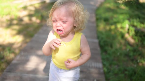 Close Up Portrait of Little Funny Cute Blonde Girl Child Toddler in Yellow Bodysuit Crying Outside